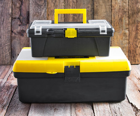 Both small and medium size portable black yellow plastic tool box with latches and handle on old wooden background.