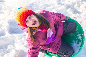 Fototapeta na wymiar A child rolls down a snowy hill. Emotion girl on a walk. Winter holiday. Outdoor games.