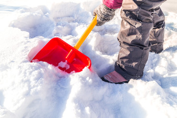 Child digs a snow shovel. Kid with his hands in mittens holds a red spade.