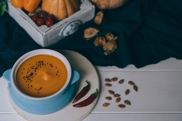 Pumpkin soup in a bowl with autumn vegetables and pumpkin seeds. Vegan soup. Vegetables cream soup and ingredients. Concept of healthy eating or vegetarian food. Toned image. Selective focus.