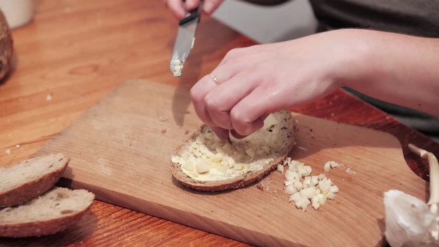 Woman's hands puts garlic on slice of bread with butter. Preparations for making a sandwich with garlic. Close Up.