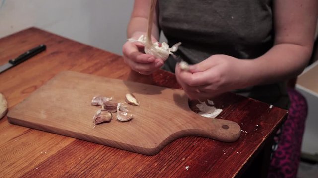 Woman's hands peeling garlic on a chopping board. Preparations for making a sandwich with garlic.