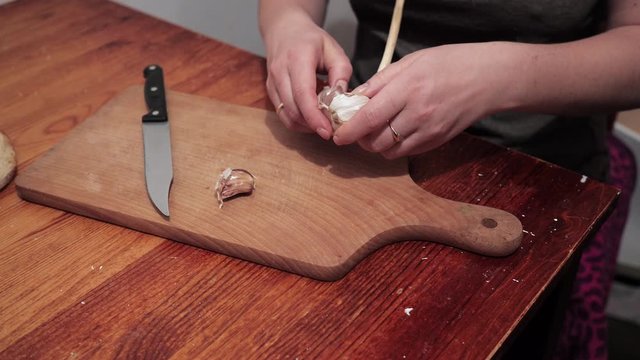 Woman's hands are starting to peel garlic on a chopping board. Preparations for making a sandwich with garlic.