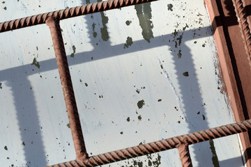 Fragment of an old window painted by white paint behind a rusty brown bars on a sunny day. Abstract background