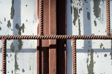 Fragment of an old window painted by white paint behind a rusty brown bars on a sunny day. Abstract background