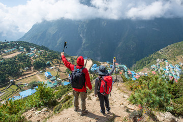 Fototapeta na wymiar Couple of tourist standing on the mountains edge and looking below to scenery view of Namche Bazaar the largest village in Khumbu region in Nepal.