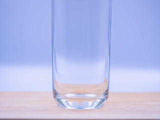 Abstract background and closeup of blank glass. Selective focus on the glass 's bottom on wooden table with blurry blue and gray background in the kitchen or living room.