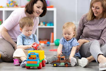 Happy two mothers with their children play at home or daycare interior