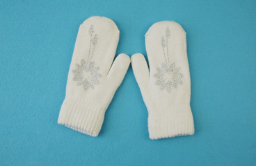 White wool mittens with rhinestone snowflake isolated on a blue background with copy space. flat lay, top view. The concept of winter clothing and accessories. Background, banner, pattern, card.