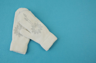 White wool mittens with rhinestone snowflake isolated on a blue background with copy space. flat lay, top view. The concept of winter clothing and accessories Winter background, banner, pattern, card.