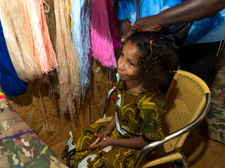 African hairdresser plaits braids with multicolored artificial strands for mixed Jamaican European ethnicity little girl. Portrait of a child with curly long hair