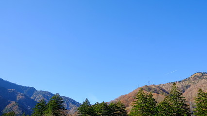 Scenic landscape view of nature forest with  mountain range hills trees and clear blue sky background in fall autumn season of kamikochi, in Hotaka Ranges, Kamikochi, Japan.