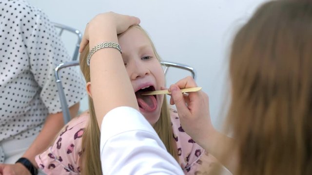 Medicine for children and healthcare concept. Portrait of child girl opening mouth at pediatrician, doctor looks at sore throat using spatula. Preventive examination of child in clinic.