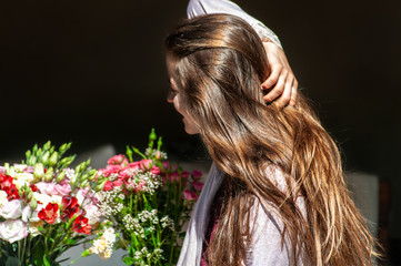 Beautiful long haired girl enjoying flowers in morning sun on dark background