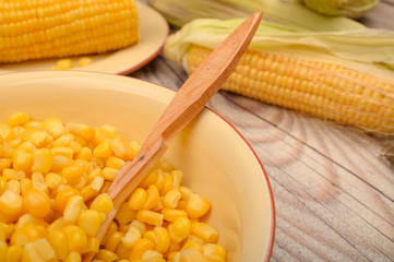 Grains of sweet corn in a plate with a wooden spoon and ears of corn on the table. Healthy diet. Fitness diet. For a sweet treat. Close up.