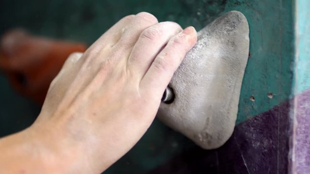 Close-up shot of manmade hold on artificial indoor wall, hand of anonymous female climber dusted with chalk grabbing it, moving away, then foot in climbing shoe stepping on it and leg swinging