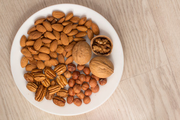 walnuts, almonds, pecans and hazelnuts on a white plate on a woodden table