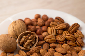 walnuts, almonds, pecans and hazelnuts on a white plate on a woodden table