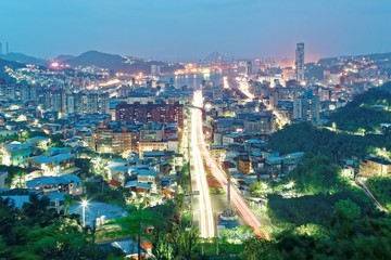 Night scenery of Keelung, a harbor city in northern Taiwan, with traffic trails on the highway, beautiful lights emitting from buildings and the busy seaport in the background