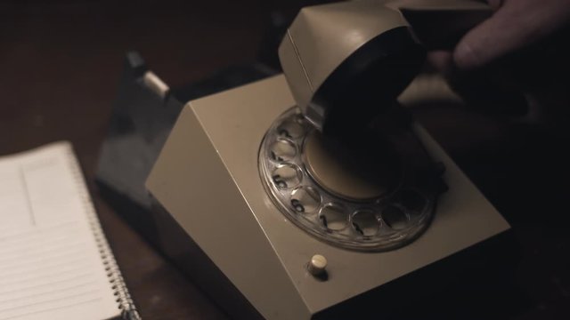 Hand picks up receiver and dials old rotary telephone in dark room