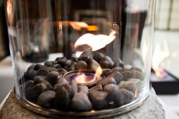 Bioethanol fueled portable fireplace burning at home, for live fire at home, no chimney and mantelpiece is needed. Liquid bio ethanol burns in cup. Round shaped glass with stones inside
