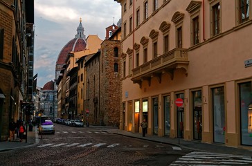 Morning scenery of a narrow cobbled street in the old town of Florence, Italy, with view of a car driving in the alley and the Dome of majestic Cathedral of Saint Mary of the Flowers in the background