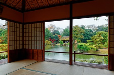 Autumn scenery of colorful foliage by the lake in a beautiful free entry Japanese garden in  Kyoto Japan, with a view thru the sliding screen doors (shoji) of a tea room in a peaceful Zen ambiance