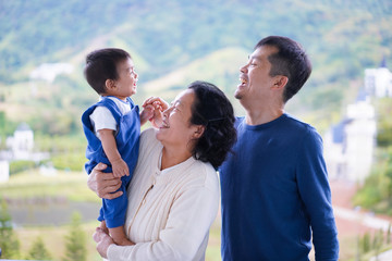 Asian grandmother is holding the little baby boy who laughing with his father , all people look happy with the moment, concept of multi generation people in asian family.