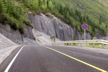 sandy cliffs along the bend of a road covered with asphalt with markings a solid line and a sign prohibiting the stoping © Dmitrii