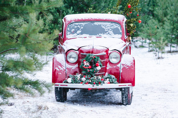 A red car with Christmas decorations and a Christmas tree is standing in a winter forest. Festive New Year concept.