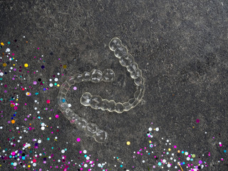 Corrector position invisible teeth over gray background, with festive confetti, give yourself a...