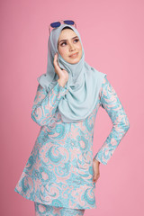 Beautiful female model wearing batik design "baju kurung" with hijab, a modern lifestyle outfit  for Muslim woman isolated over pink background. Eidul fitri fashion and beauty concept.