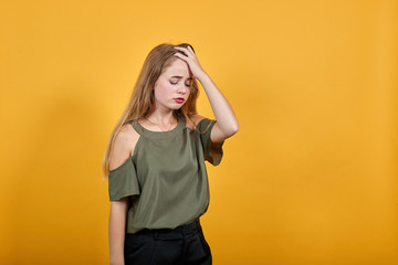 Bored young woman in casual clothes keeping eyes opened, with hand behind head isolated on orange wall background in studio. People sincere emotions, lifestyle concept.