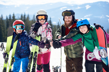 Family of four, wife, husband and two kids in sportive equipment with skis and snowboard smiling in...