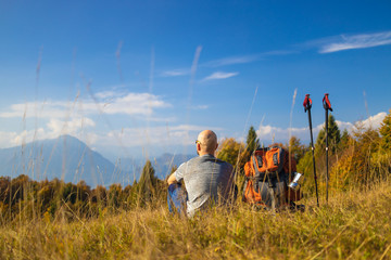 Man traveler with a backpack sits on a hill of a beautiful alpine landscape.