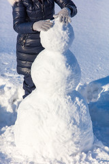 Girl sculpts a snowman in the snow