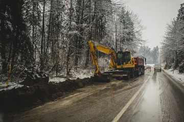 Road repair in winter. Backhoe or excavator working in front of a truck.