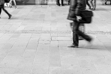 Black and white Picture of footpath as many people walk cross by. People on the street. Picture focusing on concrete with pedestrian&rsquo;s shadow on. Silhouettes and Shadows of a person on the street.