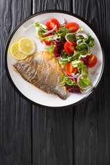 Fried gilt-head fish fillet with a side dish of vegetable salad close-up on a plate. Vertical top view