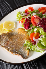 fried dorado fillet with fresh salad close-up on a plate. vertical