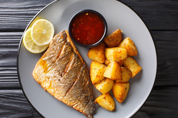 Fried gilt-head fish fillet with a side dish of potatoes and sauces close-up on a plate. Horizontal top view