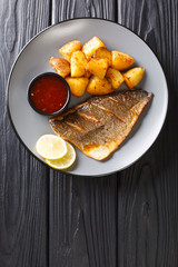 Grilled dorada filet with fried potatoes and sauces close-up on a plate. Vertical top view