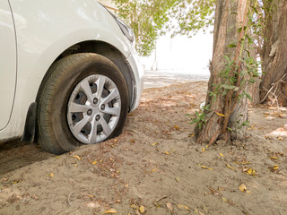 Fototapeta na wymiar punctured tire of a white modern vehicle stuck in the sand and trees 