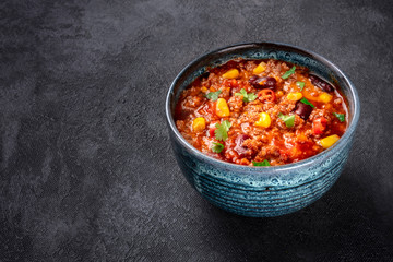 Chili con carne, a Mexican stew with beans, ground meat, corn, and chilli peppers, on a dark background with a place for text