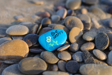 blue stone with the inscription be happy on the beach among the stones