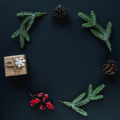 Frame of twigs, berries, cones and a gift for Christmas on a dark background