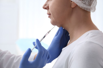 Mature woman with double chin receiving injection in clinic, closeup