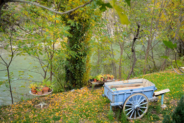 A garden near a river in South France, trees with autumnal colors. A old blue cart with wooden wheel with iron ring.