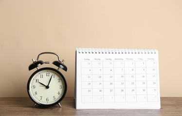 Fototapeta na wymiar Calendar and alarm clock on wooden table against beige background