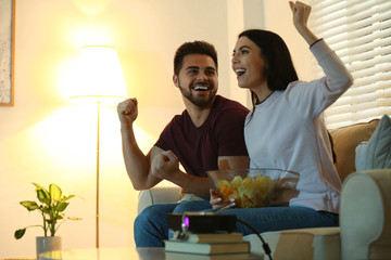Happy young couple watching TV using video projector at home